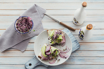 Healthy vegetarian bruschettas with bread, micro greens, cheese, cucumbers and red onion on light rustic wooden table