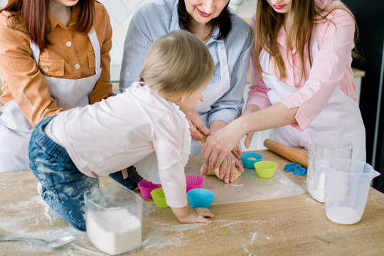 Happy women in white aprons baking together. Close-up photo of women hands and little baby preparing dough for baking muffins. Family, cooking, baking and people concept