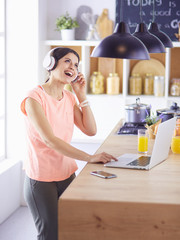 Young woman in kitchen with laptop computer looking recipes, smiling. Food blogger concept.