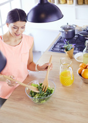 Smiling young woman mixing fresh salad in the kitchen.