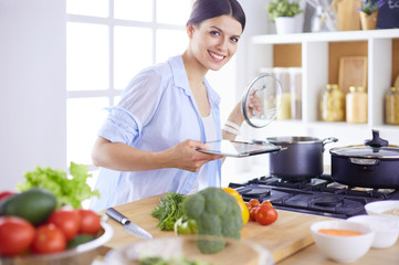 Young woman using a tablet computer to cook in her kitchen.