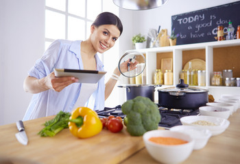 Young woman using a tablet computer to cook in her kitchen.