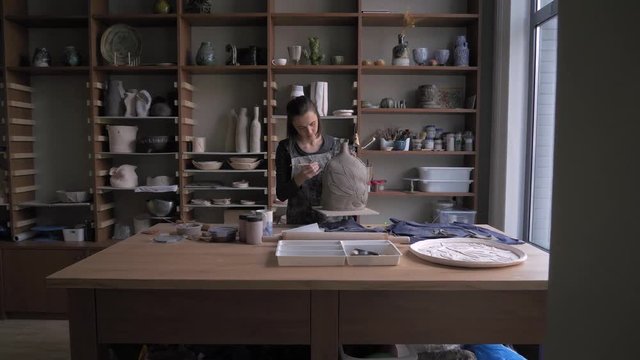 a beautiful woman ceramist removes excess clay from her product dolly shot