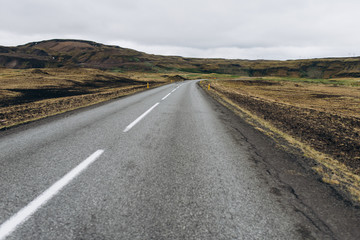 The road between the mountains and the hills. Asphalt road in Iceland. The road is in the field.