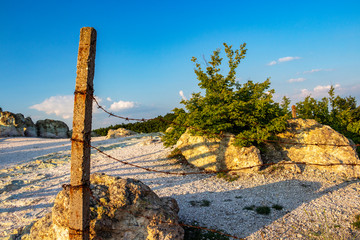 Weathered concrete pillar with rusty barbed wire on a natural background, the fence of the Stone Mushrooms near Beli Plast village, Bulgaria - obrazy, fototapety, plakaty