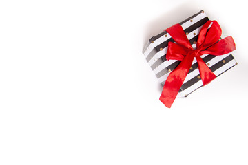 Gift or present box in white and black stripes with a red ribbon bow isolated on white table top view. Minimal flat lay composition for sales, birthday, mother day or christmas. copyspace