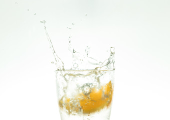 Slice the orange slice in a glass of water and make a spray on a white background. water spray in the air. a slice of citrus drops in a glass spray.