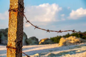 Weathered concrete pillar with rusty barbed wire on a natural background, the fence of the Stone Mushrooms near Beli Plast village, Bulgaria, close partial view