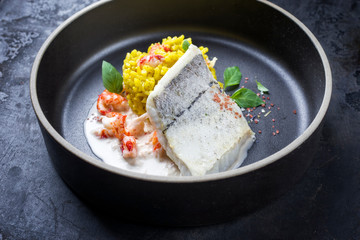 Fried haddock filet with saffron rice and shell prawns in crab sauce as closeup on a modern design bowl