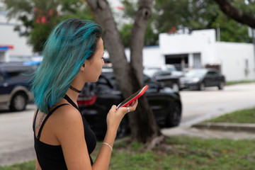 Portrait of a girl holding a mobile phone in hands talking on speakerphone. Side view. Girl with blue hair. 