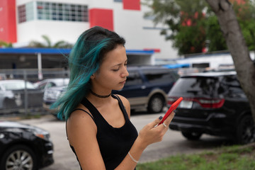Portrait of a girl holding a mobile phone in hands talking on speakerphone. Side view. Girl with blue hair. The girl is sad.