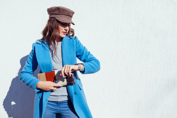 Young woman looking on watch, holding handbag and wearing blue coat. Spring female clothes and accessories. Fashion