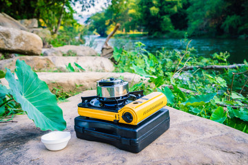 Picnic gas stove and aluminum teapot for boiling water during camping near the river