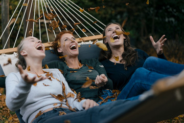 Carefree mother with two teenage girls throwing autumn leaves in hammock in garden