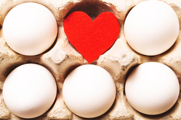 White eggs and red heart in carton box.