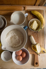 Ingredients to prepare a bunch of banana muffins are displayed over a wooden board,too view, natural light