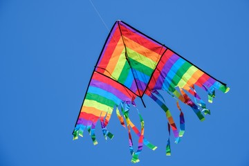 Kite flying in blue sky summer background,  white tail.
