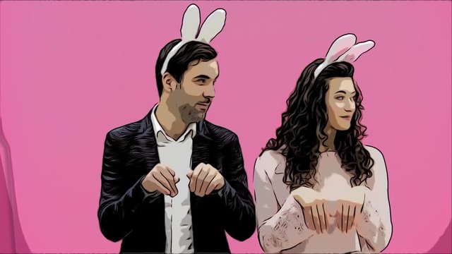 Young couple standing standing on pink background. During this time, they are dressed in rabble ears. Looking at each other, talk and smile. Easter Concept.