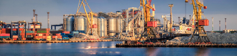 Loading grain to the ship in the port. Panoramic view of the ship, cranes, and other...