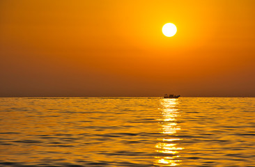 Palinuro sunset with perfect alignment of the sun, its reflection in the water and a passing dinghy