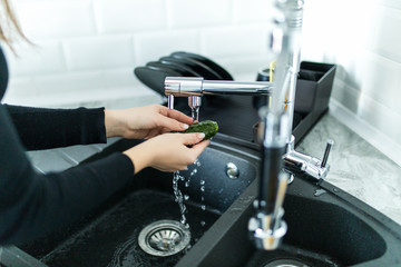 Woman washing cucumbers in kitchen sink close up.