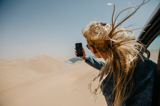 Namibia, Walvis Bay, Namib-Naukluft National Park, Sandwich Harbor, woman leaning out of car window taking cell phone picture