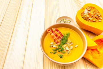 Homemade autumn hot pumpkin cream soup with smocked bacon and seeds. Raw pumpkin, fresh chives, dill, salt in spoon on wooden background, close up.