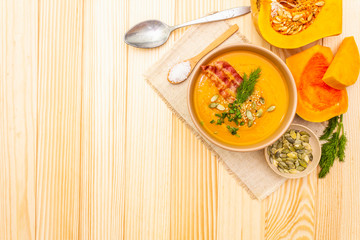 Homemade autumn hot pumpkin cream soup with smocked bacon and seeds. Raw pumpkin, fresh chives, dill, salt in spoon, vintage linen cloth on wooden background, top view copy space.