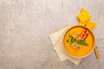 Homemade autumn hot pumpkin cream soup with smocked bacon and seeds. Raw pumpkin, fresh chives, dill, salt in spoon, vintage linen cloth on stone background, top view copy space.