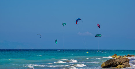 Unidentified kitesurfers practicing Kitesurfing at Aegean Sea beach on the peninsula Prasonisi, Rhodes. Colorful kites on the sea shore.