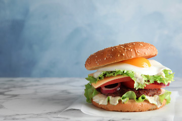 Tasty burger with fried egg on marble table against color background, space for text