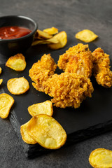 Chicken fried strips with baked potato slices on a black table. Homemade fast dinner.
