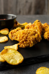 Chicken fried strips with baked potato slices on a black table. Homemade fast dinner.