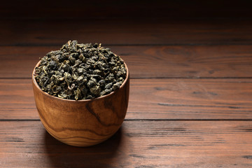 Bowl of Tie Guan Yin oolong tea leaves on wooden table. Space for text