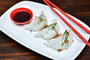 Traditional asian rice dough steamed dumplings with stuffing, spring onion and fried chips decor, served with spicy chilly sauces