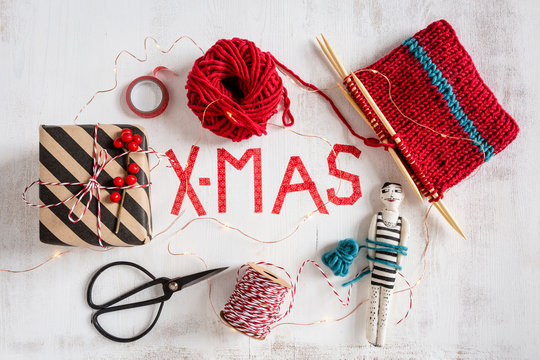 Wrapped Christmas present, knitting, scissors and small puppet on white wood