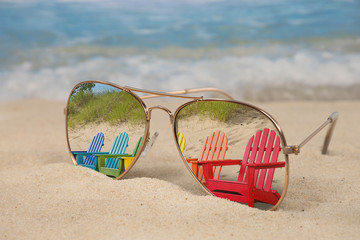 colorful row of Adirondack chairs reflected in aviator sunglasses in beach sand