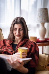 Beautiful woman reading a book at home, enjoying some good read and drinking coffee or tea