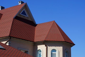 red tile on the roof of the attic of a large private house with a window against the blue sky