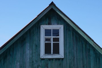 Fototapeta na wymiar old green wooden loft with white window against the blue sky