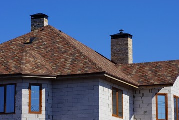 facade of the house of gray brick with windows under a brown tiled roof against the blue sky