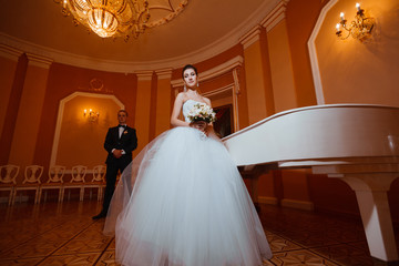 Newlyweds near the piano.In love with the luxurious interior.Wedding photo