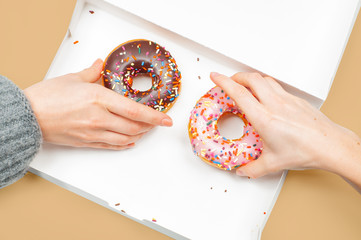 Female hands is taking two last donuts in box on pastel background.