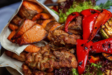Mixed grill meat, fried vegetables and grilled salmon fish fillets decoration in warm dish. Assorted delicious grilled kebab served with herbs on platter. Restaurant menu plate