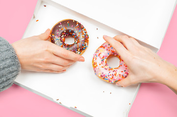 Female hands is taking two last donuts in box on pastel pink background.