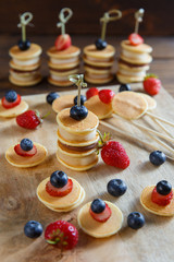 Fruit, berry and pancake canapes on wooden table