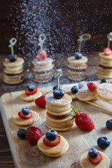 Fruit, berry and pancake canapes on white wooden table