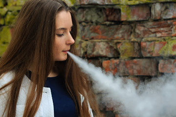 Vape teenager. Young pretty white girl in white cardigan smoking an electronic cigarette opposite...