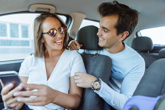 Happy Couple In Car With Man On Back Seat And Woman With Cell Phone On Front Passenger Seat