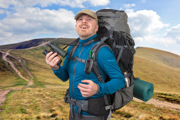 Happy man traveler with binoculars in hand on mountains background